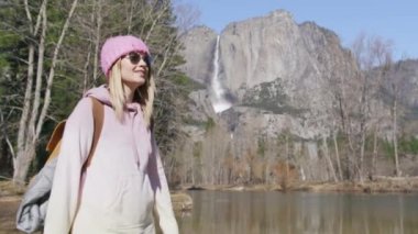 Pembe şapkalı bir kadın, sonbahar çam ormanlarında sırt çantasıyla dolaşıyor.