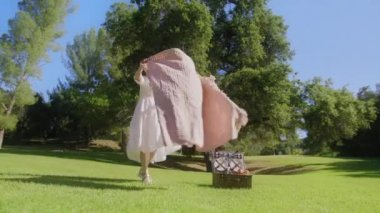 Yeşil Park yaz gününde piknik battaniyesini seren güzel bir kadın.