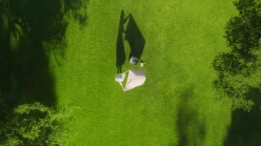 Beyaz elbiseli 4K hava kadını yeşil park günbatımında piknik battaniyesini seriyor.