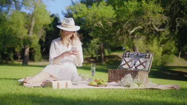 Красная камера замедленной съемки Красивая женщина сидит, используя смартфон в зеленом парке — стоковое видео
