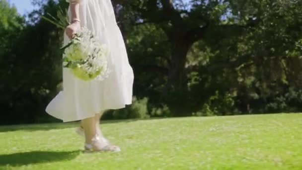 Câmera vermelha mulher câmera lenta andando com saco de palha e flores no parque verde. — Vídeo de Stock