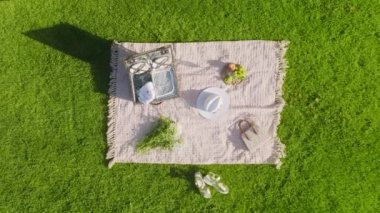 Aerial 4k top down footage stylish picnic blanket with basket, flowers white hat