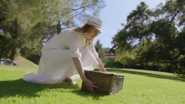 Happy smiling woman in white hat having lunch with picnic basket in green park — Stock Video