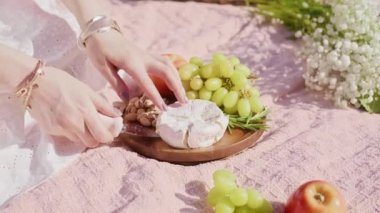 Ahşap tabakta peynirli, üzümlü, elmalı, şam fıstıklı peynir yiyen kadın.