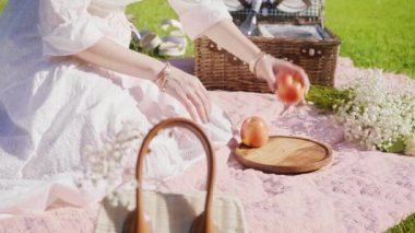 Kırmızı kamera ağır çekim kadın çimlerin üzerinde oturuyor, piknikte meyve yiyor.