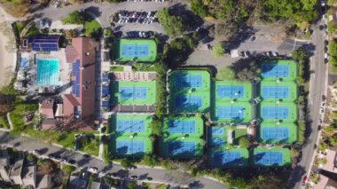 Yüksek açılı yukarıdan aşağıya, park alanında havuzu olan fitness kulübündeki tenis kortlarında tenis oynayan insanların üzerinde hala havadan drone atışı var. Pahalı gayrimenkul evlerindeki Calabasas Dinlenme Merkezi