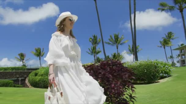 在阳光明媚的夏日 一个慢动作微笑的女人走过热带岛屿 长长的白色飘扬的裙子 金发在海风中飘扬 享受夏威夷红镜头6K暑假的愉快游客 — 图库视频影像