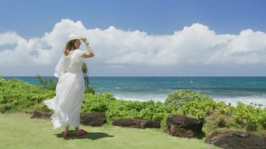 Maksimum beyaz boho tarzı elbise giymiş Amerikalı bir kadın yaz tatilinde deniz mavisi okyanusa bakıyor. Tropik Hawaii adasında rüya gezisi. Fotokopi alanı olan yaz turizminin yavaş çekim arkaplanı, RED 6K