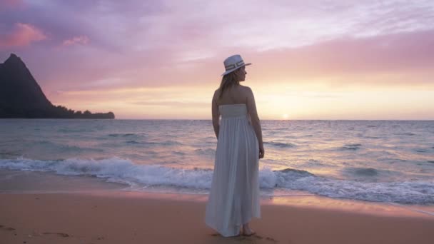 遅い動きのバックビュー美しい夕日を見て海の波で長い白いドレスのエレガントな女性は驚くほど穏やかなピンク 紫の色合いで着色されます 異国の島での夏休み — ストック動画