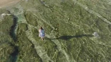 Plaj elbiseli gülümseyen kadının üstündeki hava, sığ sularda kalıyor. Saf, şeffaf dalgalar kıyıya vuruyor, Hawaii adası macera gezisi, yaz sabahı Haena plajı. 