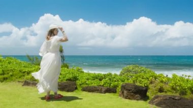 Maksimum beyaz boho tarzı elbise giymiş Amerikalı bir kadın yaz tatilinde deniz mavisi okyanusa bakıyor. Tropik Hawaii adasında rüya gezisi. Fotokopi alanı olan yaz turizminin yavaş çekim arkaplanı, RED 6K