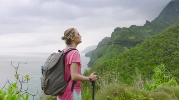 在多云的海岸背景上 一个女人走过绿色的丛林山 夏威夷考艾岛Napali海岸Kalalau小径的慢动作电影自然景观 美国背包自然旅游 — 图库视频影像