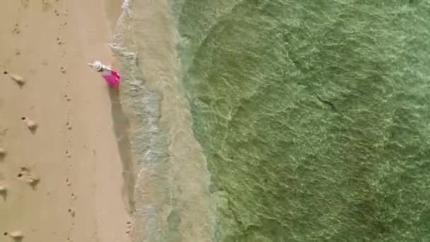 ハワイ島の海岸で熱帯のビーチを歩く遅い動きの女性 陽射しが水面を波打つフレア 鮮やかなピンクのドレスとエレガントな帽子で旅行者の女性に続くドローン — ストック動画