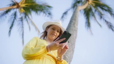 Kumsalda akıllı telefon cihazıyla cep telefonu tutan mutlu beyaz kadın. Gülümseyen genç blogcu yeni sosyal medya aboneliği yapıyor, internetten satın alıyor, uygulamalarla ürünler sipariş ediyor