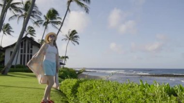 Yaz tatilinde tropikal Hawaii adasında eğlenen çekici genç bir kadın ellerini kaldırıp plajda uçuyor ve manzaralı okyanuslara bakıyor. Kumsal tatil köyü RED 'de mutlu, rahat kadın.