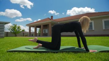Spor giyimli zayıf, güzel bir kadın yeşil çimenlikteki evin arka planında kardiyo eğitimi ve yağ yakma çalışması yapıyor. Yüksek kalite 4k görüntü