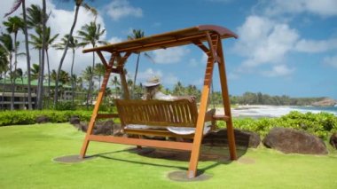 Mutlu yaz tatili hayalleri. Lüks bir tatil köyünde sallanan zarif bir bayanın manzarası. Okyanus manzaralı. Tahta salıncaktaki sarışın kadın Hawaii Adası 6K 'da tatilin tadını çıkarıyor.