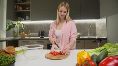 Akşam yemeği hazırlarken domates doğrayan bir kadın görüntüsü. Güzel beyaz kız mutfakta yemek pişirirken gülümsüyor. Yüksek kalite 4k görüntü