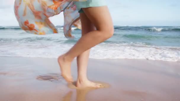 在夏天的海滩上 嬉闹的女人穿着在海风中飘扬的衣服 在白茫茫的浪花中飞溅 在暑假旅行中 年轻女子细腿在美丽的夏威夷海岸散步时的慢镜头特写 — 图库视频影像