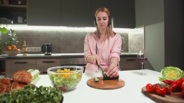 여자가 음악을 들으면서 오이를 자르는 부엌에서 샐러드를 만들어요 고품질 — 비디오