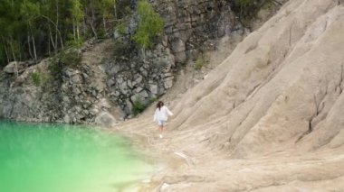 Yeşilimsi gölün kumlu sahillerinde gezinen bir kadının havadan görünüşü. Kadın turist, arka planda bir ormanla yapay taş ocağının içinde yürüyor. Yüksek kalite 4k görüntü