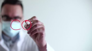 Doktor cam tahtaya Covid-19 sembolü yazıyor. Bulanık bir geçmişi olan, tıbbi maskeli beyaz bir adam. Yüksek kalite 4k görüntü