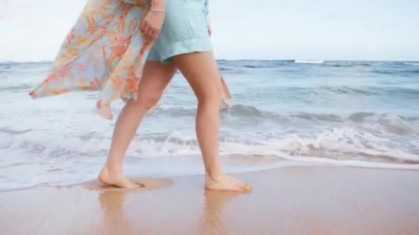 穿着艳丽海滩衣服的女人在阳光下被海风吹拂着 年轻女子细腿的慢动作特写走在风景优美的白沫般的海浪中 浪花飞溅 在她的两脚之间散落 — 图库视频影像