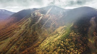 Franconia Notch Park, New Hampshire, New England, ABD. Sonbahar orman yapraklarıyla kaplı dağların havadan görünüşlü yeşillikleri. Bombardıman dağı kayak merkezi güneşli bir sonbahar gününde 4K