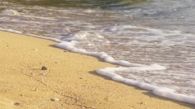 Sahilde altın gün batımı, kumlu plaja doğru ilerleyen köpüklü dalgaların yavaş çekimi. Kırmızı kamera, güneşli yaz gününde sinemada çekildi. Sahil manzaralı bir ada tatili..