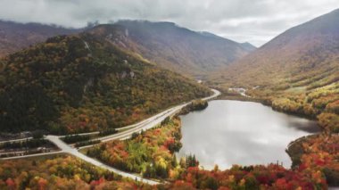 Sonbahar günü Cannon Dağı kayak merkezinde Echo Gölü manzaralı, Franconia Notch Park, ABD. Turistler dağ gölü boyunca renkli sonbahar ormanı arka planıyla sinematik yeşilliklerin yanından geçiyorlar.