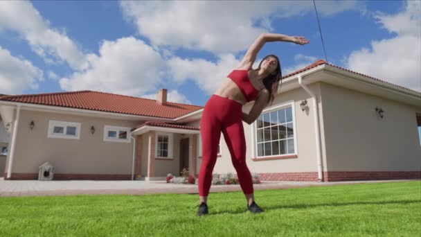 女运动员进行热身运动 同时用胳膊进行能动的动作 女人伸展在室外 后面是漂亮的房子 高质量的4K镜头 — 图库视频影像