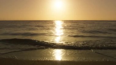 Dramatik deniz gündoğumu. Görkemli yanan gökyüzü, arka planda parlayan altın dalgaları yansıtıyor. Adanın kumsalında altın gün batımı, yavaş çekim parlak dalgalar kumlu sahile doğru yuvarlanıyor alçak güneş ışığı altında