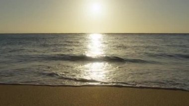 Mükemmel bir yaz tatili geçmişi ve ufukta altın bir gündoğumu var. Sihirli gökyüzü parlak altın dalgalara yansıyor. Yavaş çekim, parlak dalgalar parlayan güneş ışığının altında kumlu sahile yuvarlanıyor.