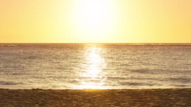 Güzel yaz tatili arkaplanı, üzerinde yazı alanı olan altın gün batımı. Sihirli gökyüzü parlak altın dalgalara yansıyor. Yavaş çekim, parlak dalgalar parlayan güneş ışığının altında kumlu sahile yuvarlanıyor.