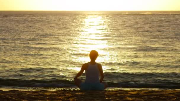 女性瞑想 自然の風光明媚な黄金の夕日の禅のヨガの瞑想の練習 ヨギの女の子蓮のポーズ 健康的なライフスタイル 瞑想の概念に座っている スローモーション女性トレーニング屋外でビーチ — ストック動画