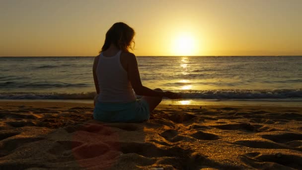 海と砂の穀物で輝く黄金の風光明媚な夕日で映画のビーチに座っている一人の女性 スローモーションのバックビューでは 指を介して砂をこぼす女性を検討 時間を背景に飛んでいく — ストック動画