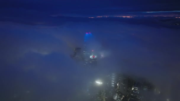 空中の鳥の目は霧の間にサンフランシスコの都市の未来的なスカイラインを表示します 夜の街の青の光に照らされた映画の雲に覆われた夜のダウンタウンの上空を飛ぶドローン — ストック動画