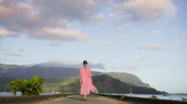 Yavaş çekim kamerası, Hawaii adası manzarasının üzerinde mavi gökyüzünde bulutlarla sinemanın tadını çıkaran kadını takip ediyor. Hanalei 'deki iskelede bir gezgin. Seyahat tatilinde açık hava yaşam tarzı