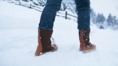 Kırsal kesimde taze beyaz karın yanından geçen kadın botlarını kapat. Sahne yavaş çekim, kış görüntüsü RED kamera 6K. Soğuk bir günde, arka planda orman geçmişi olan sinematik kış harikalar diyarı
