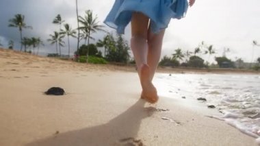 Plajda yaz tatilini kutlayan lüks oteldeki çıplak ayaklı kadını kapat. Okyanus meltemiyle süslü elbiseli bir kız tatilin tadını çıkarıyor. Yaz arkaplanı ağır çekimde, Tropikal Hawaii