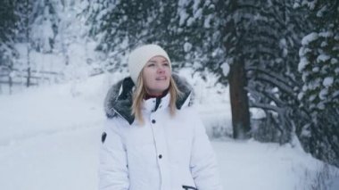 Portrait of positive smiling woman walking in winter wonderland forest and looking around with admiration of nature beauty. Cinematic winter landscape in Aspen countryside. Christmas vacation footage
