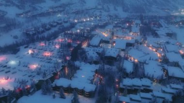 Kış gecesi dağlar, hava manzarası. Büyülü kış, Noel köyü manzarası. Aydınlatılmış dağlık bir şehir. Karla kaplı, beyaz dağlar, kayak merkezi. 4K gecesi Aspen tatil köyünde.