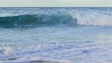 Parlayan dalgalara yansıyan görkemli güneş ışığı. Hawaii adasındaki kumlu sahile doğru yavaş çekimde su sıçratan dalgalar. Yumuşak pastel renklerde dramatik mavi okyanus dalgaları, kopyalama alanı için doğa arkaplanı