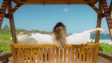Happy young woman feeling freedom, spreading arms like a flying bird on ocean breeze with cinematic island beach landscape. Scenic summer travel background slow motion footage, beautiful dream trip