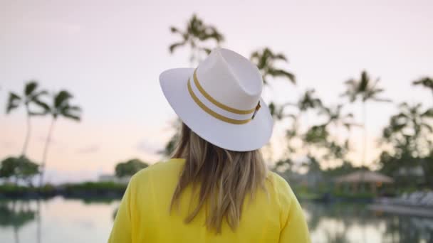 Tourist woman in straw hat enjoying summer vacation at sea beach. Close up girl looking green palms in sunset sky. Traveler in white hat relaxing on happy holiday at luxury hotel. Tropical spa resort