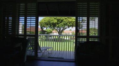 Beach style apartment with island shutters on french door windows. Walking to balcony lanai with sun-beds and beach furniture. Scenic summer tropical nature landscape. Summer vacation on dream island