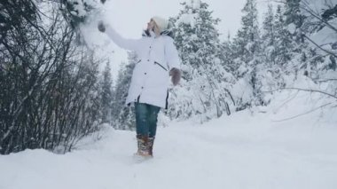 Slow motion front view of young excited woman touching the pine tree branch covered by fresh snow falling down. Woman having good times outdoors on snowy winter day. Winter wonderland RED camera shot
