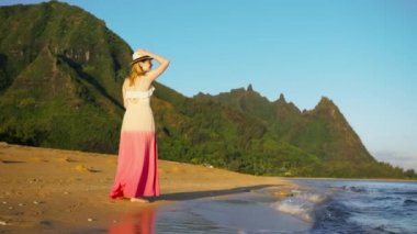 Slow motion cinematic shot on RED camera traveler woman walking in golden sunrise hour by scenic coast landscape. Woman enjoying breathtaking Hawaii nature with amazing green mountain peaks at summer
