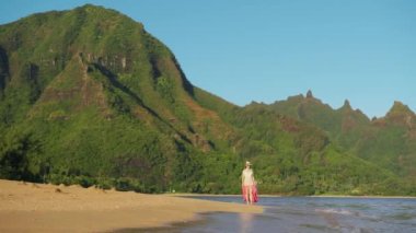 Young tourist hipster girl on refreshing morning walk at Hawaii golden beach against beautiful tropical green mountain landscape. 4K Slow motion RED camera footage shot on paradise dream Hawaii island