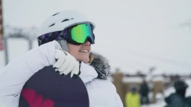 Sağlıklı beyaz dişlerle gülümseyen kendine güvenen bir kız. Beyaz kasklı, renkli snowboard gözlüklü beyaz atletik kadını kapatın. Güzel genç insan yüzü, kayak merkezinde kış gününün tadını çıkarıyor.